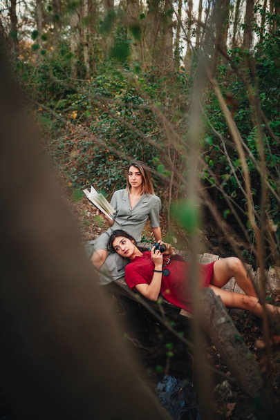 Nuoret naiset lukemassa kirjaa ja ottamassa kuvia metsässä
 - Valokuva, kuva