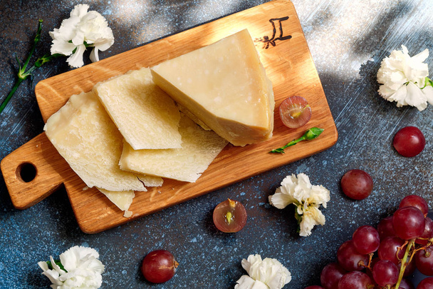 Pieces of parmigiano reggiano or parmesan cheese on wood board on dark background - Photo, image
