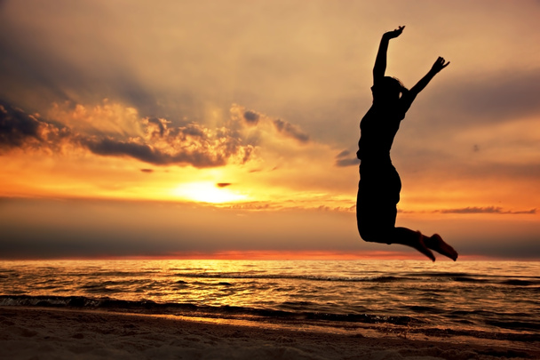 Щаслива жінка стрибає на пляжі на заході сонця
 - Фото, зображення