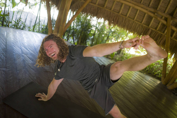 mode de vie portrait de jeune homme attrayant et heureux dans le style hipster yogi faire des exercices de yoga sur tapis à la belle cabane de bambou asiatique étirant à l'esprit l'équilibre et de bonnes vibrations
 - Photo, image