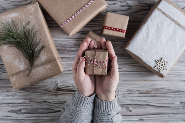 Female packing small gift. Cardboard box in craft paper, christmas rope and tree on the rustic wood planks background. DIY. - Photo, image