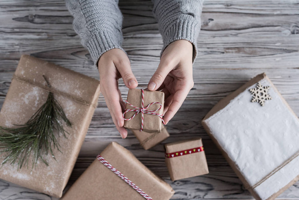 Female packing small gift. Cardboard box in craft paper, christmas rope and tree on the rustic wood planks background. DIY. - Φωτογραφία, εικόνα