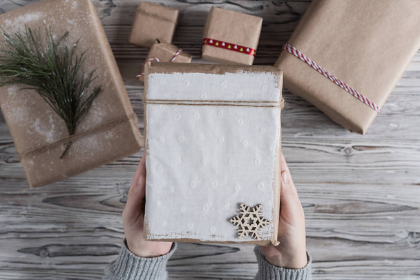 Female packing gifts. Cardboard box in craft paper, christmas rope and tree on the rustic wood planks background. DIY. - Photo, image