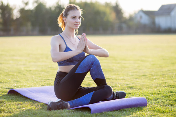 Молодая спортсменка в положении йоги медитирует в поле на солнце
 - Фото, изображение
