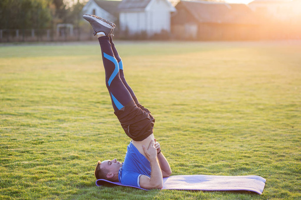 Young sportive man doing exercises in morning field outdoors. - Photo, Image