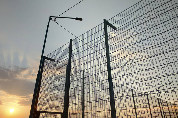 Высокая проволочная сетка забор в ограниченной области на голубом фоне неба
. - Фото, изображение