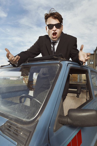 Man in zwart pak gebaren op zijn mooie retro auto - Foto, afbeelding