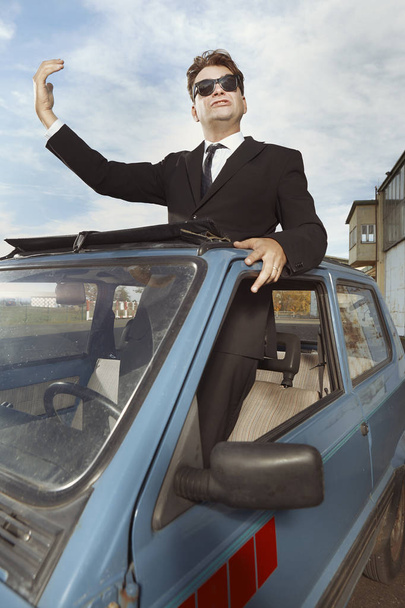 Man in black suit gesturing on his lovely retro car - Fotó, kép