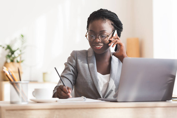 Afro Secretary Talking On Phone And Taking Notes At Workplace - Valokuva, kuva