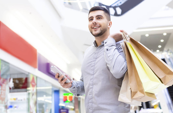 Young man with cellphone and shopping bags waiting girlfriend - Photo, Image