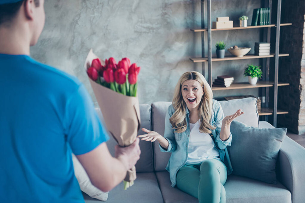 Portrait of her she nice attractive charming pretty ecstatic cheerful cheery wavy-haired girl sitting on divan receiving floristry red flowers at modern industrial loft brick style interior living - 写真・画像