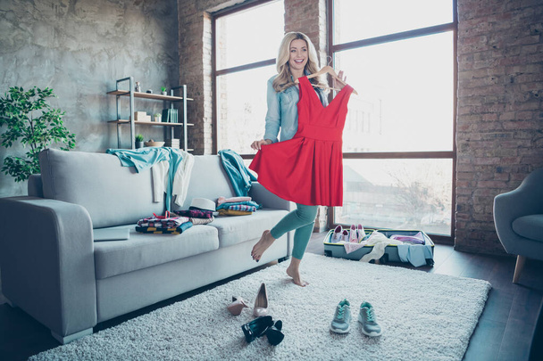 Full length body size view of nice attractive charming pretty fashionable cheerful cheery wavy-haired girl trying red dress preparing wardrobe for voyage at modern industrial loft brick style interior - Photo, image