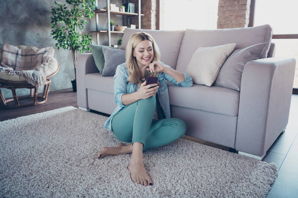 Portrait of her she nice attractive lovely charming cheerful cheery wavy-haired lady sitting on carpet sending sms to husband at modern industrial loft brick style interior living-room - Фото, изображение