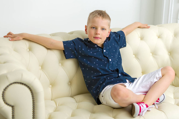 小さな男の子が白いソファの上にスタジオに座っています。コンセプス - 写真・画像