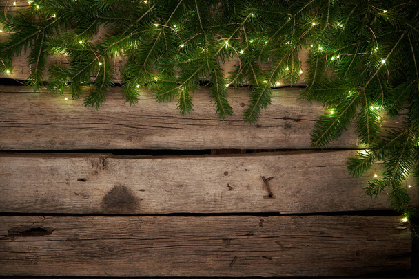 Green Christmas tree branches with lights on rough weathered wooden planks - Photo, Image