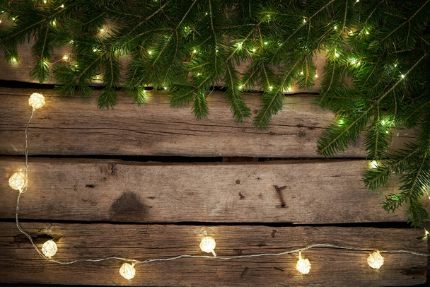 Green Christmas tree branches with lights on rough weathered wooden planks - Photo, Image