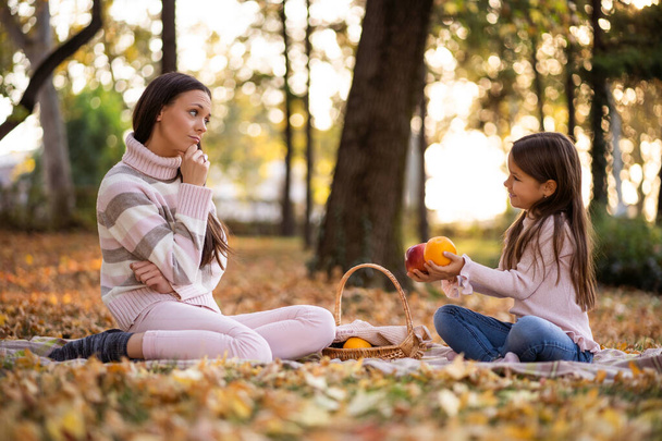 Mother and daughter having picnic in park in autumn. - Фото, изображение