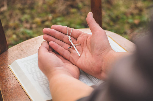 Жінка тримає хрест в руці на тлі Біблії
.  - Фото, зображення