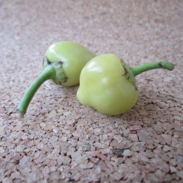 Twee kleine hete groene paprika 's op bruine kurkondergrond. Kruidige voedselcomponenten. - Foto, afbeelding