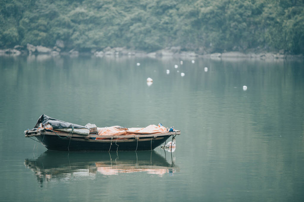 Mała drewniana łódź wiosłowa odpłynęła na szmaragdowe zielone wody w pobliżu Cat Ba Village w Ha Long Bay, Północny Wietnam - Zdjęcie, obraz