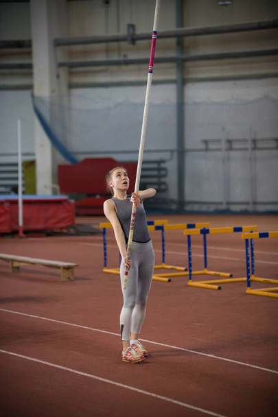 Pole vaulting indoors - young woman is standing with pole in hands - Photo, Image