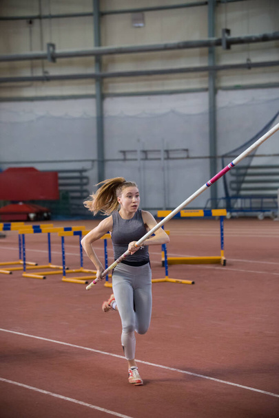 Pole vaulting indoors - young sportive woman in leggins running with a pole in the hands - Photo, Image