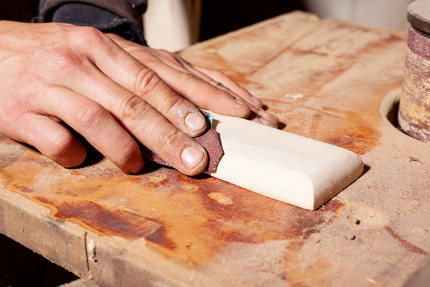 τρίβοντας ένα ξύλινο αντικείμενο με γυαλόχαρτο, ο ξυλουργός γυαλίζει μια ξύλινη λεπτομέρεια - Φωτογραφία, εικόνα
