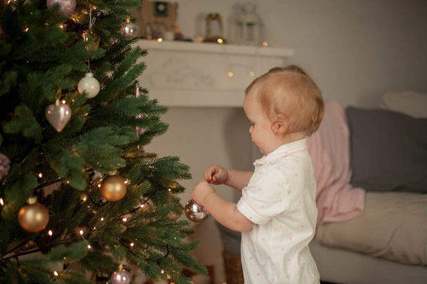 Petite fille mignonne de 2 ans en pyjama décore un arbre de Noël. Noël. Nouvel An. Des vacances. Confortable
. - Photo, image