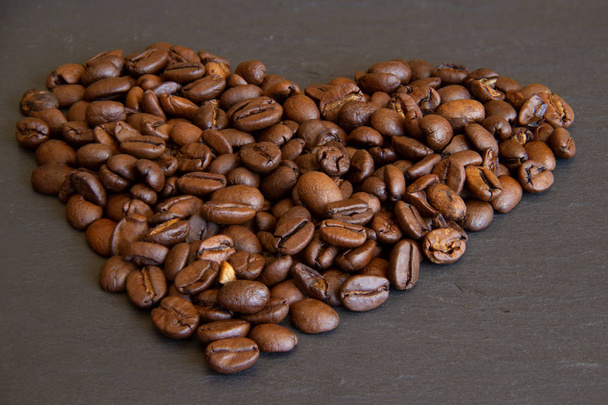 Κόκκοι καφέ σε σχήμα καρδιάς σε ένα μαύρο πιάτο σχιστόλιθου. Καφές αγάπη, καφές Εραστές Concept. Αντιγραφή χώρου για κείμενο. καβουρντισμένα, καφέ φασόλια - Φωτογραφία, εικόνα