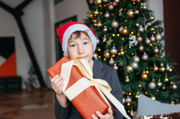 Houkutteleva hauska teini poika tummat hiukset santa hattu lahjapaketti joulukuusi tausta
 - Valokuva, kuva
