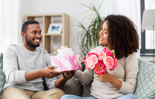 happy couple with flowers and gift at home - Φωτογραφία, εικόνα