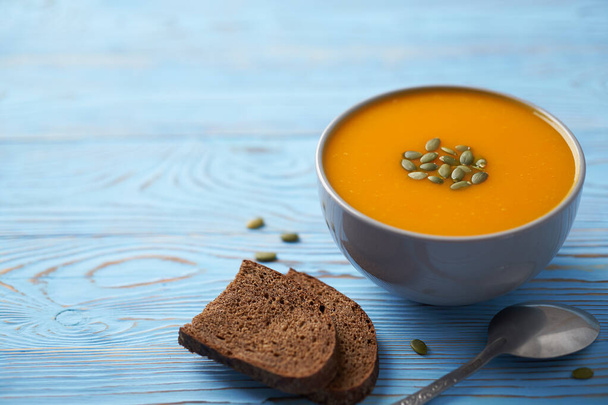 Sopa de puré de calabaza y zanahoria en un tazón gris adornado con semillas. Fondo de madera azul, composición de otoño
. - Foto, Imagen