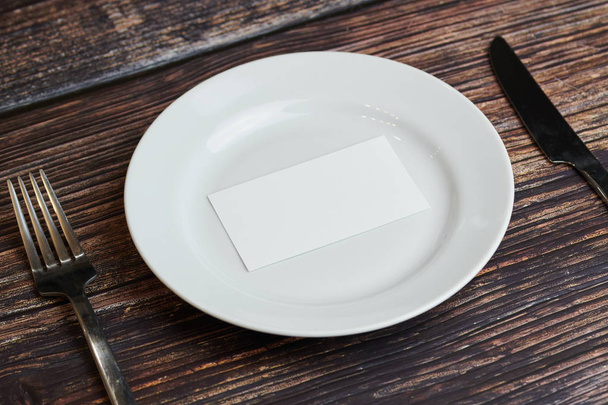 Empty plate on table with cutlery and blank business card, top view. Message for visitor of restaurant or cafe. Business lunch without tips concept. - Foto, Imagem