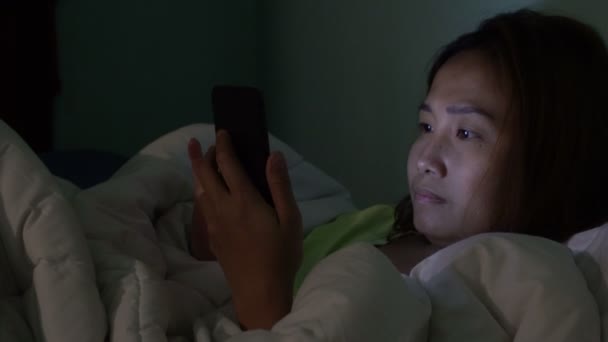 Asian woman playing game on smartphone in the bed at night - Кадры, видео