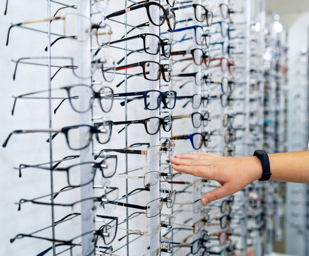 Row of glasses at an opticians. Eyeglasses shop. Stand with glasses in the store of optics. Woman's hand showes glasses. Presenting spectacles. - Foto, Bild