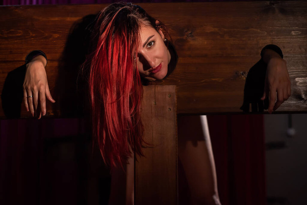 A redhead woman is imprisoned in a wooden pillory during sex games. BDSM Erotic fantasies.Subordination. Toys for adults. - Foto, afbeelding