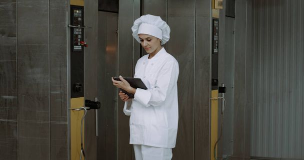 Femme mûre, vérifier la machine à four industriel prendre quelques notes sur la tablette
 - Photo, image