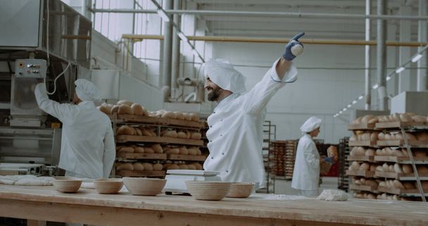 Divertente panettiere danzante in un'industria di panetteria mentre faceva l'impasto per cuocere un pane che danzava pieno di energia accanto a lui
 - Foto, immagini