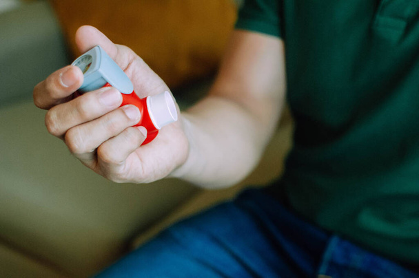 A young man is holding an asthma inhaler device while sitting on a couch - Foto, immagini
