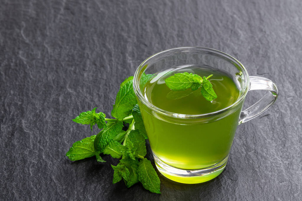 Green mint tea in clear glass cup on black stone background  - 写真・画像