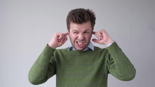 Portret van een ernstige jonge man die betrekking hebben op beide oren met handen geïsoleerd op de grijze achtergrond - Video