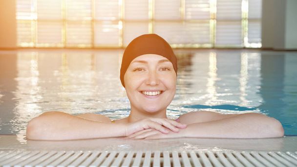 Young woman in cap looking at camera and smiling in swimming pool. - Foto, afbeelding