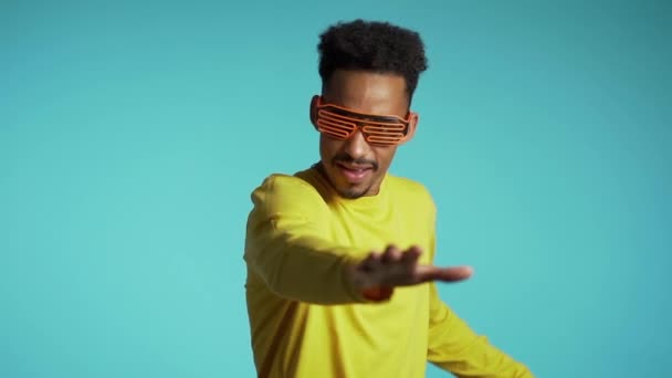 Mixed race man in glowing glasses dancing on blue studio background. Night club, party, positive lifestyle concept. Slow motion. - Filmagem, Vídeo