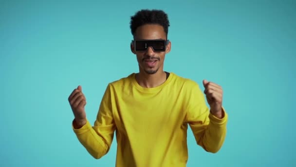 African man in glowing neon glasses moving to the music rhythm on studio background. Dancing positive comic guy. Slow motion. - Filmmaterial, Video