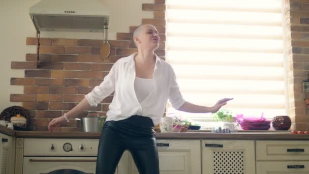 medium shot. young amazingly emotional bald woman dancing in the kitchen at home - Footage, Video