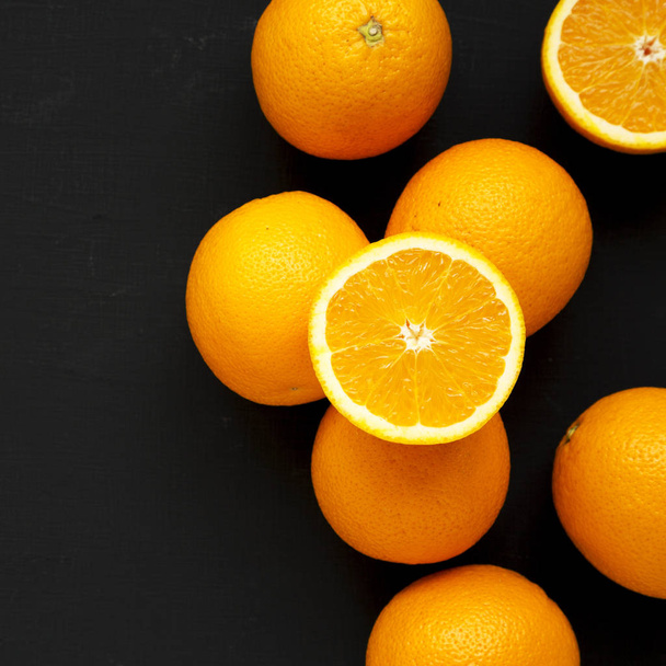 Dojrzałe organiczne pomarańcze na czarnej powierzchni, widok z góry. Płaskie łoże, łoże - Zdjęcie, obraz