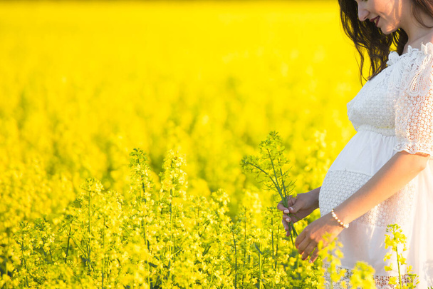 Pregnant girl on a yellow background. looks at his stomach, imagines his unborn child. Maternity concept - Foto, imagen