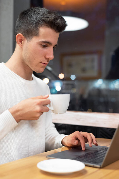 junger Mann arbeitet an seinem Laptop in einem Café, junger Student tippt am Computer.  - Foto, Bild