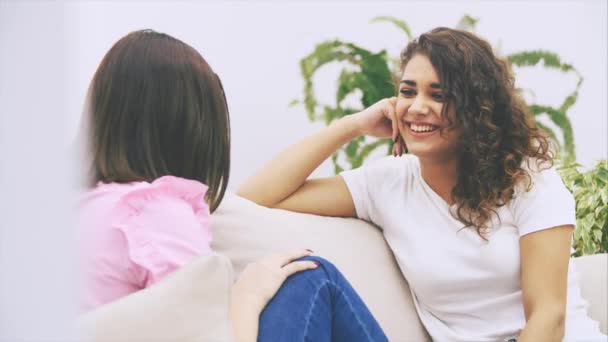 Happy friends talking carelessly, laughing, sitting on the sofa. Young brunette girl sitting back to the camera, blurred. - Filmagem, Vídeo