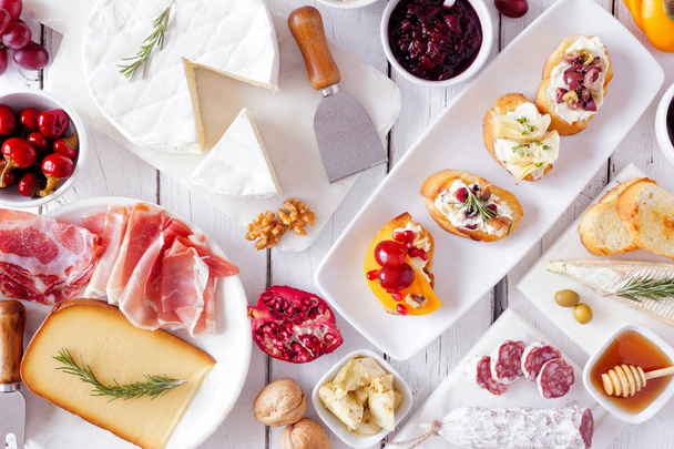 Party appetizers of assorted cheeses, meats and crostini. Top view on a white wood background. - Фото, зображення